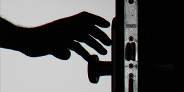 Silhouet van een hand bij een deurkruk en deurslot