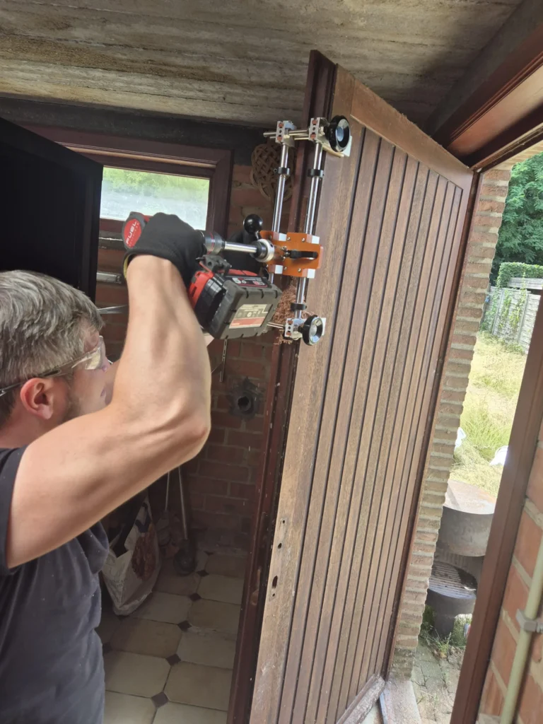 Vakman bewerkt een open houten deur met gereedschap voor slotmontage