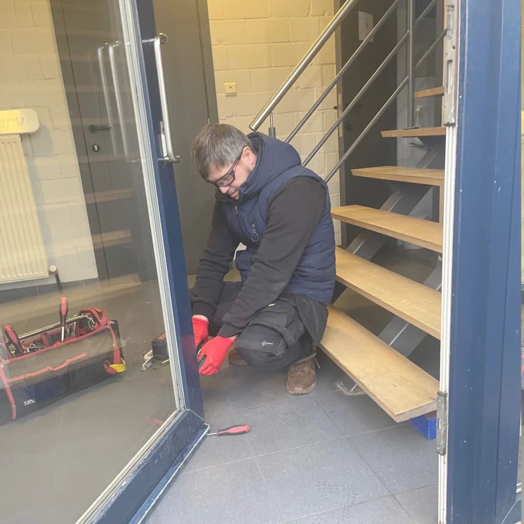 Technieker met gereedschap bij de onderzijde van een open glazen deur